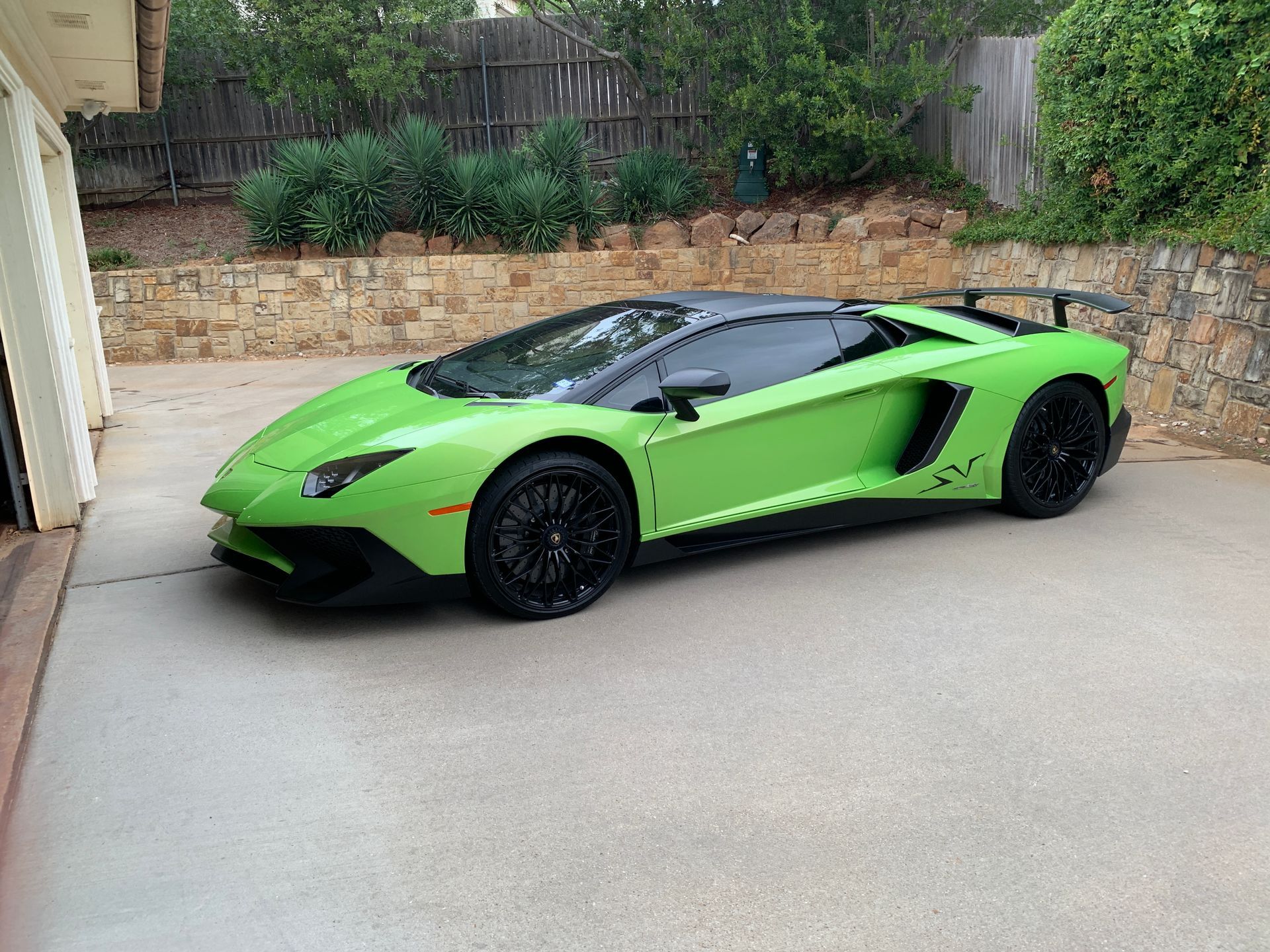 Green Lamborghini Aventador parked on a concrete driveway, with a black roof and wheels.