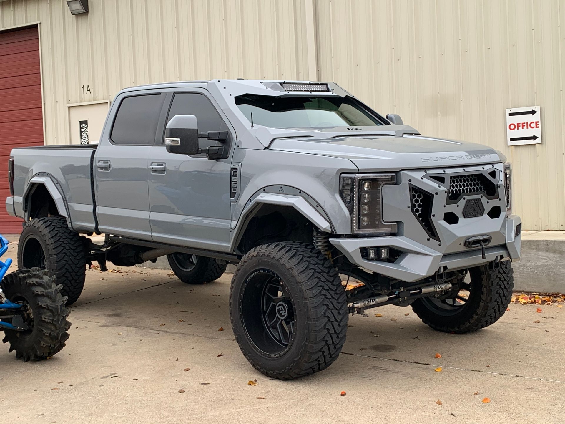 Gray lifted pickup truck with large black tires parked outside a building.