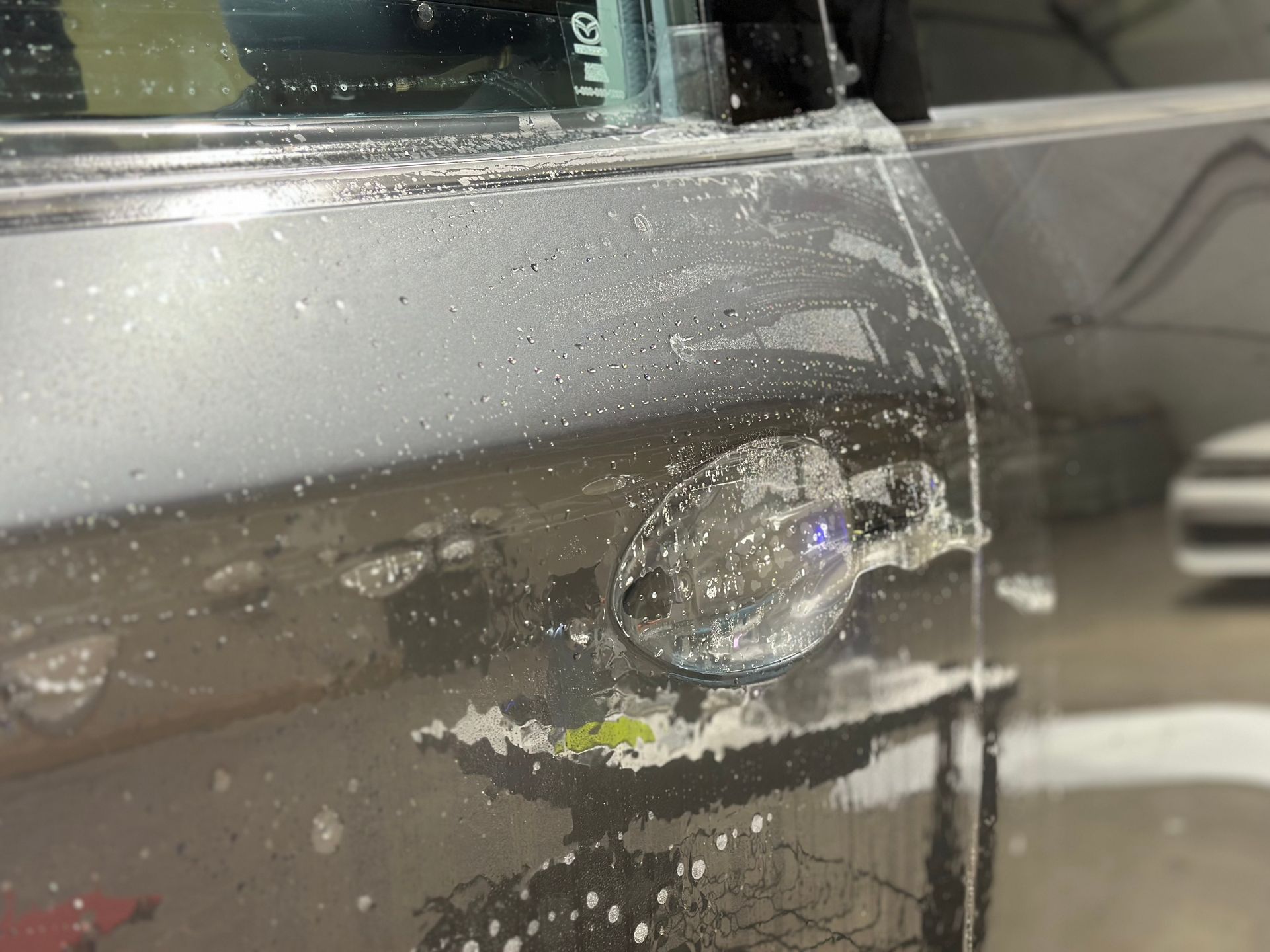 A car door covered in soapy suds, being washed.