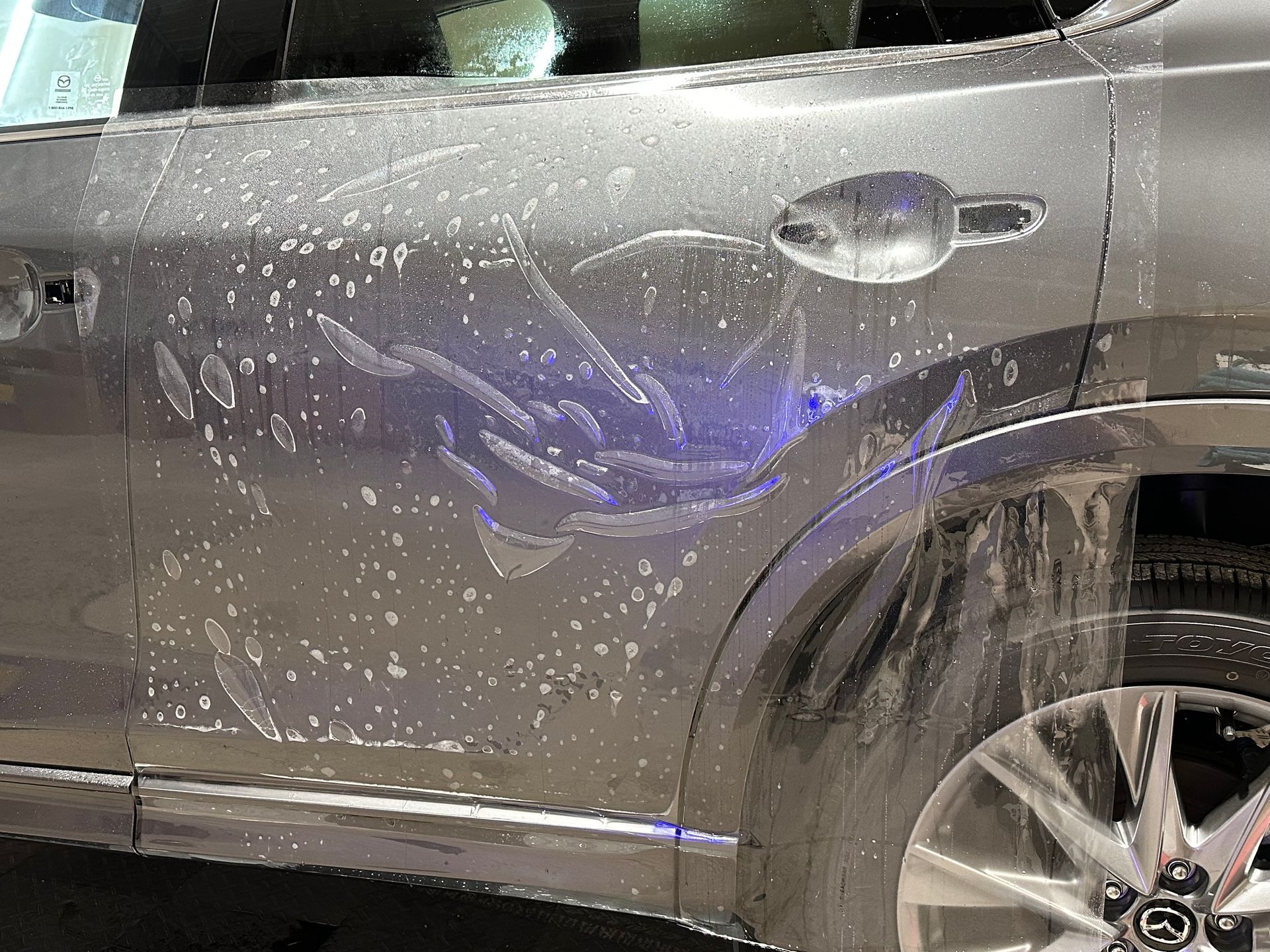 Gray car door covered in soapy water, with a silver door handle and tire visible.