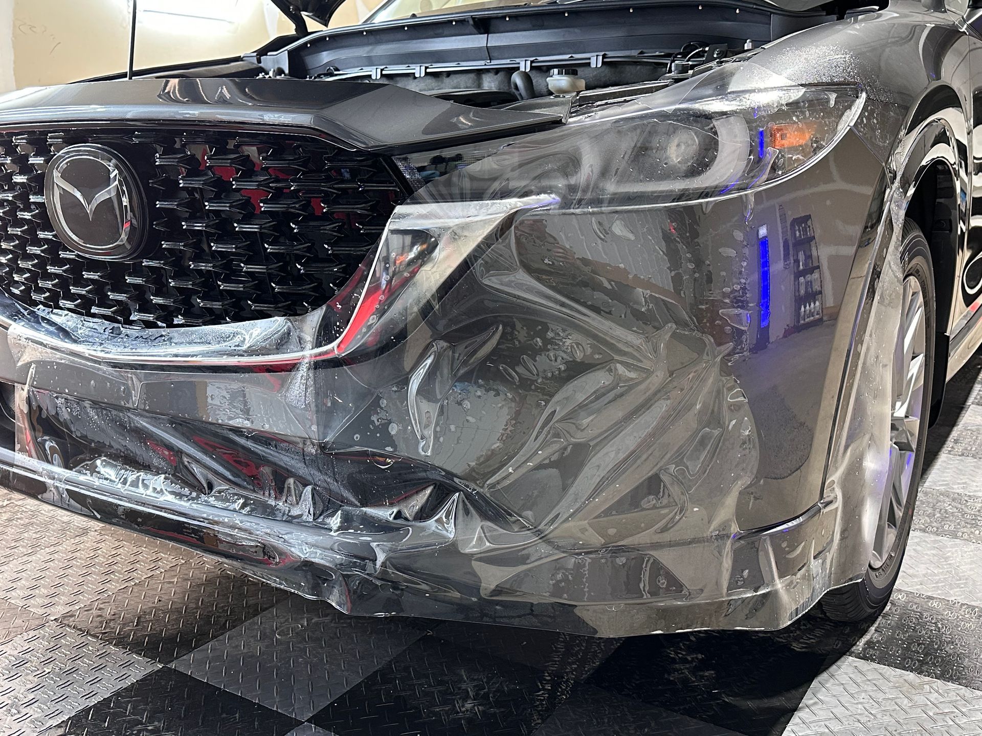 A shiny black Mazda CX-5 with protective film on the front bumper and grill.