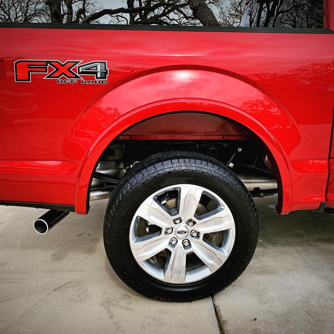Red Ford F-150 truck, showing the rear wheel and FX4 emblem on the fender. Silver wheel and black tire.