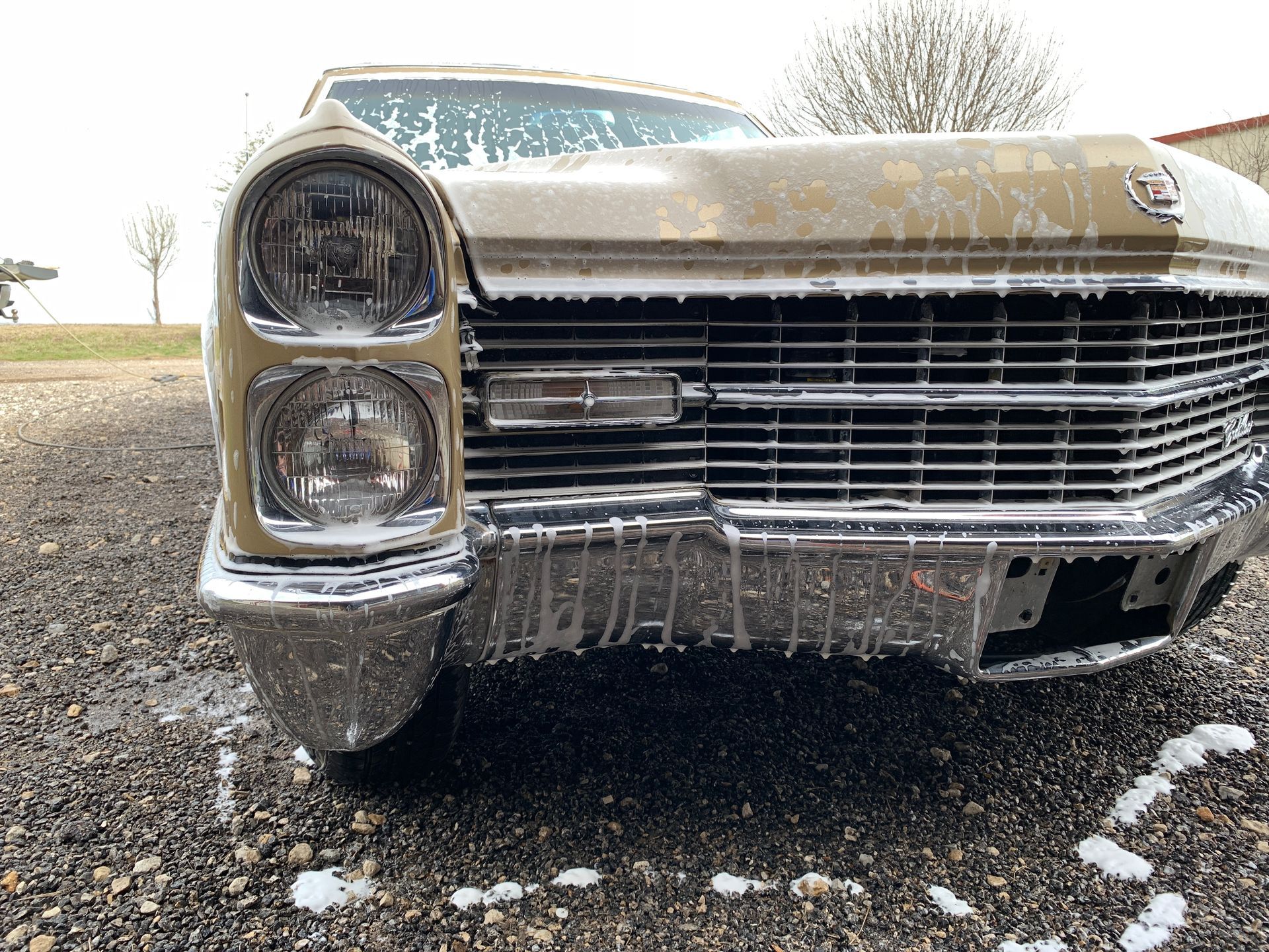 A vintage Cadillac covered in soap, being washed outdoors on a snowy day.