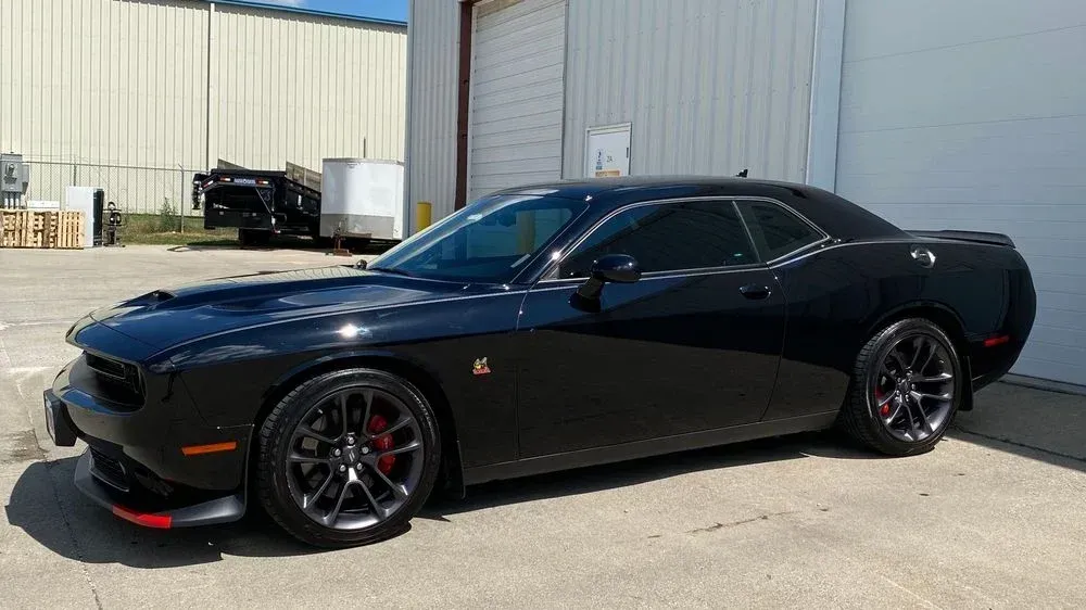 Black Dodge Challenger coupe parked outside. Red accents, tinted windows, dark rims, sunny day.