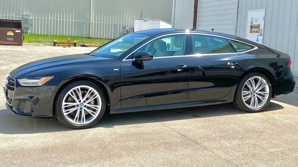 Black Audi A7 parked on concrete, with a gray building in the background on a sunny day.
