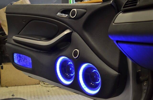 Car door panel with blue LED lights illuminating speakers. Black leather.