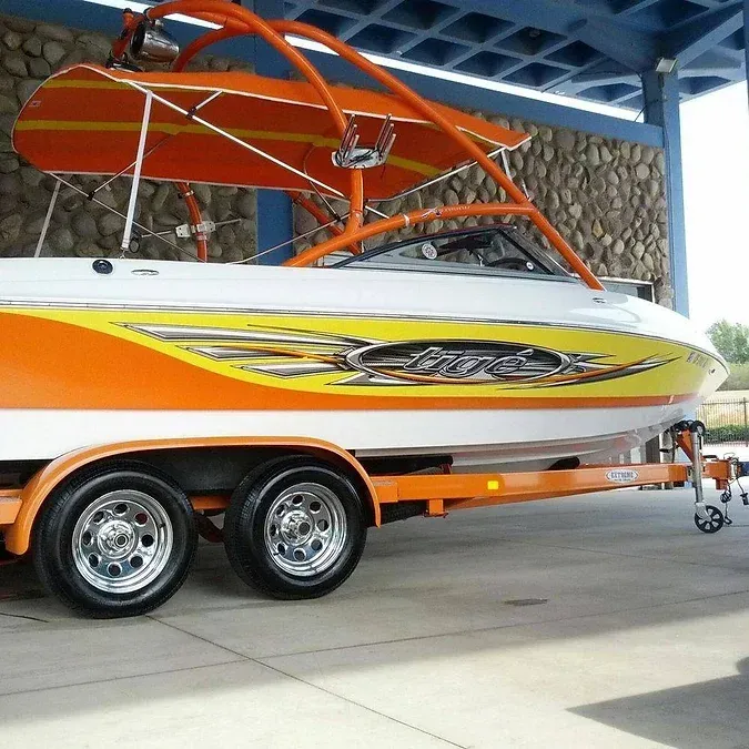Orange and white speedboat on a trailer with a matching orange roll cage, parked.