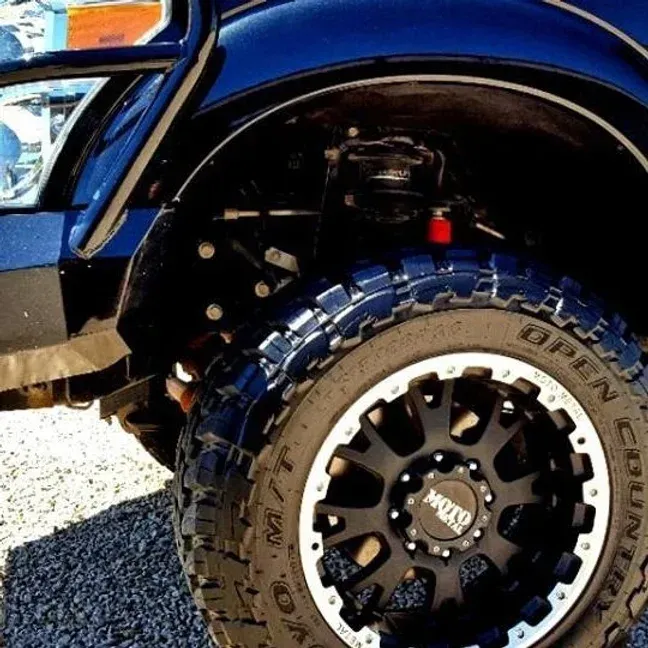 Black truck's front tire and wheel with a custom black and silver rim, under the fender.