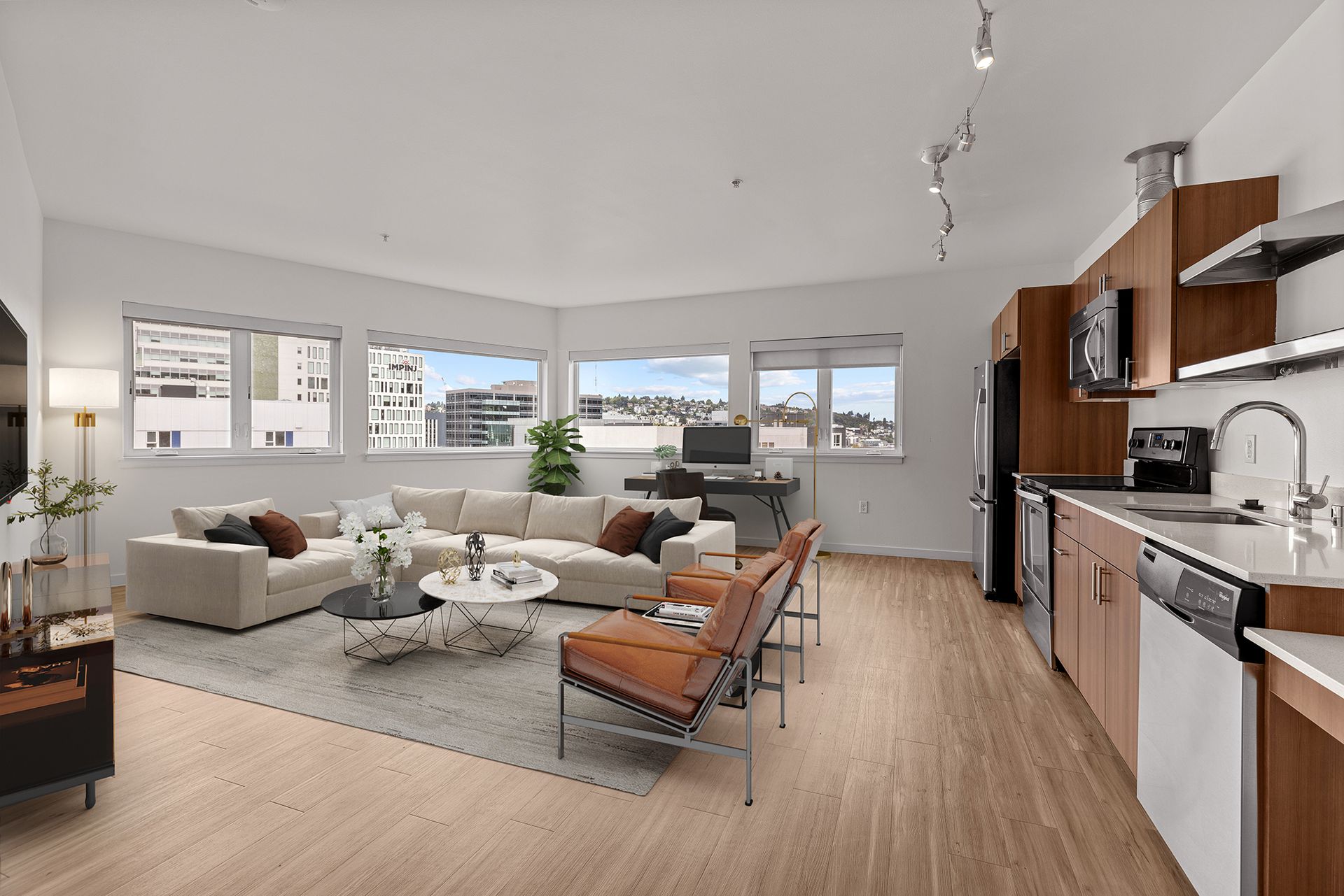 A modern, spacious apartment interior with a living area, kitchen, and windows with city views. Furnishings include a large sectional sofa, chairs, and a desk.