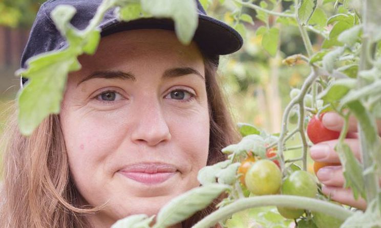 Community gardener Jacqueline, posing with ripening cherry tomatoes on the vine