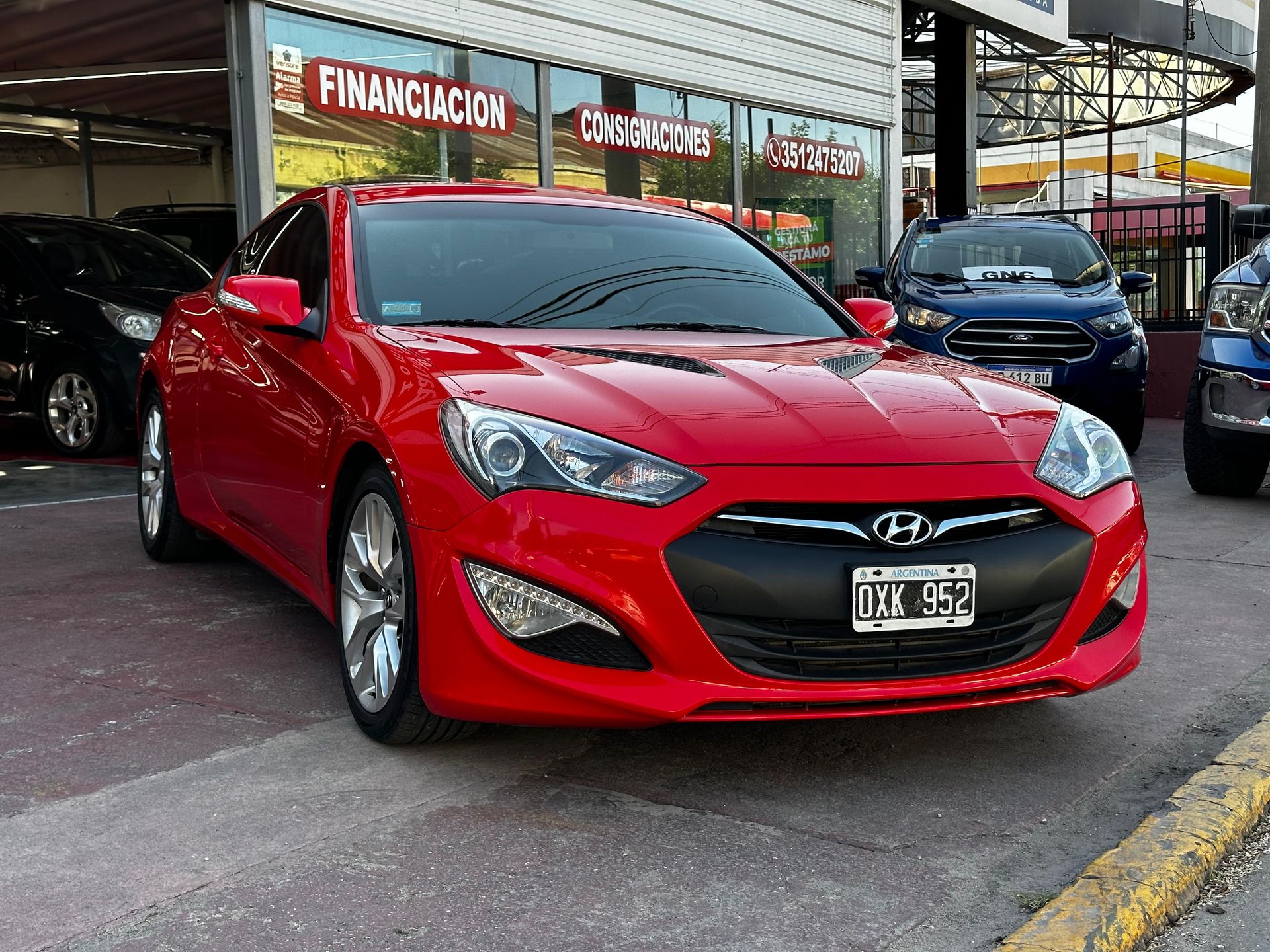 Un coche rojo está aparcado delante de un concesionario de automóviles.