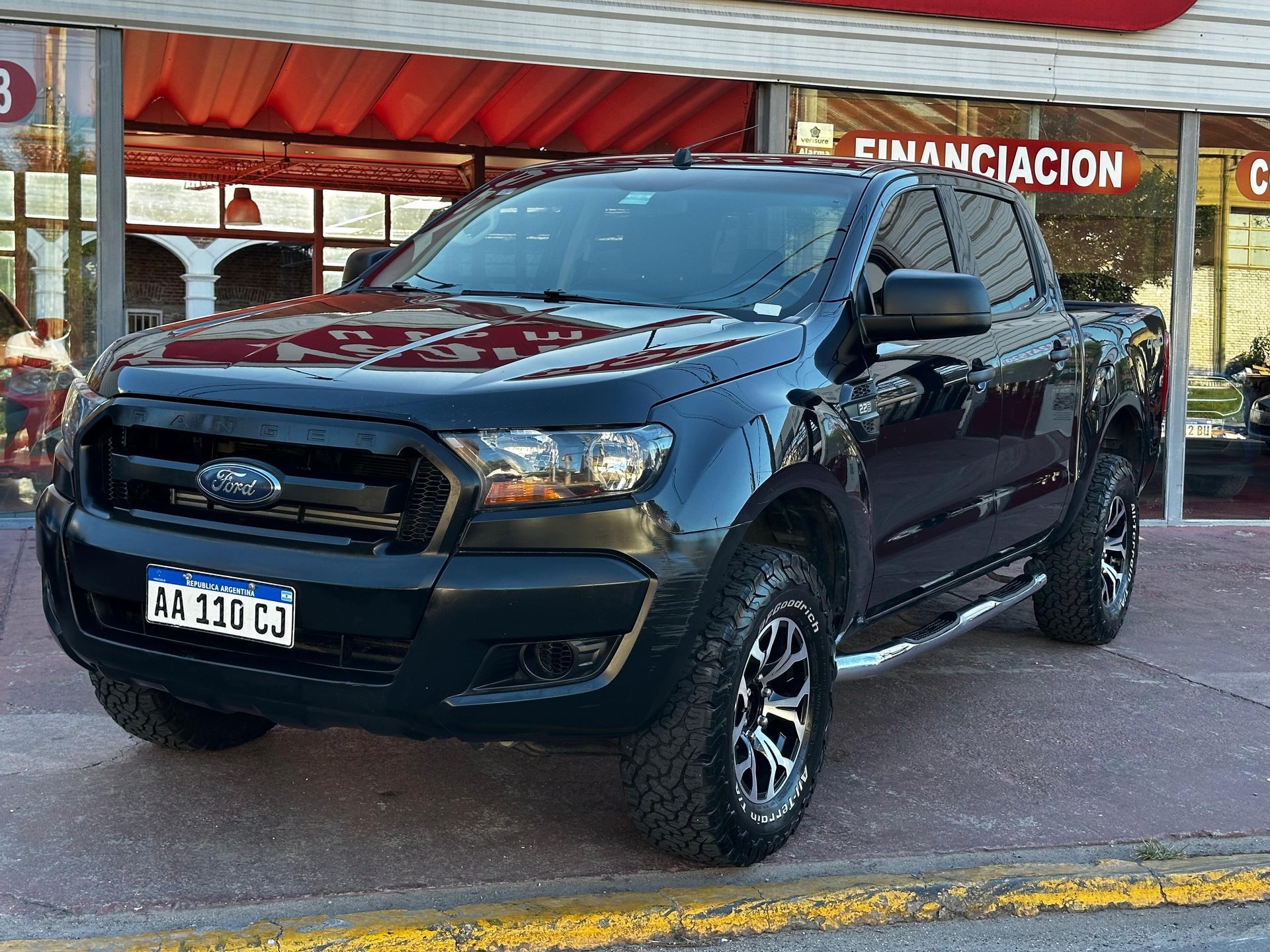 Una camioneta Ford Ranger negra está estacionada frente a un concesionario de automóviles.