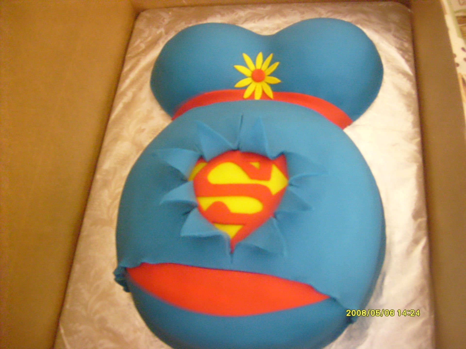 Blue plush toy with a red-and-yellow Superman-style emblem in a cardboard box