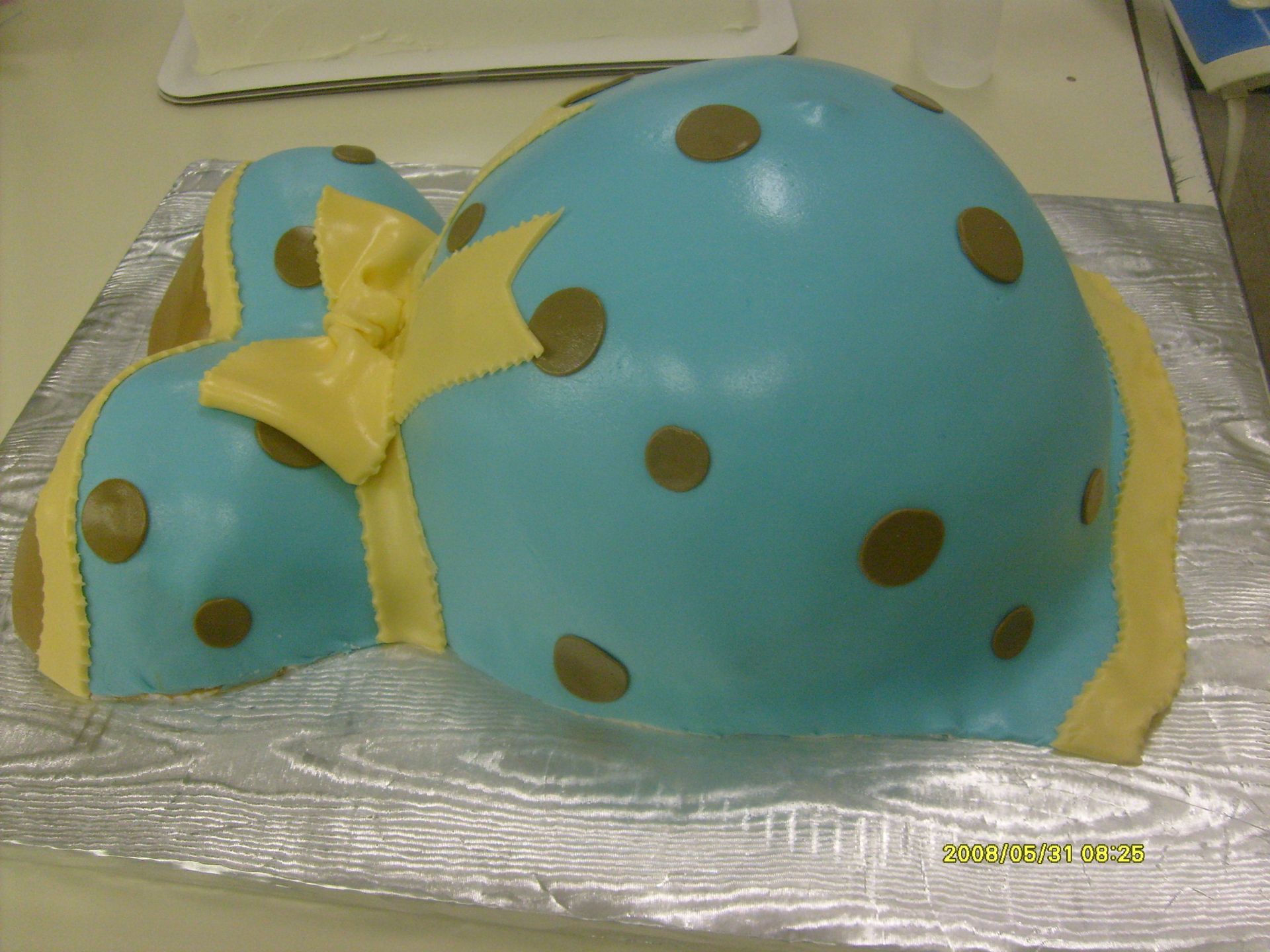 Blue polka-dot cake shaped like a dome, decorated with yellow ribbon and bow on a silver board