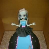 Blue-haired doll in a black and pink dress, standing with arms outstretched against a cardboard background