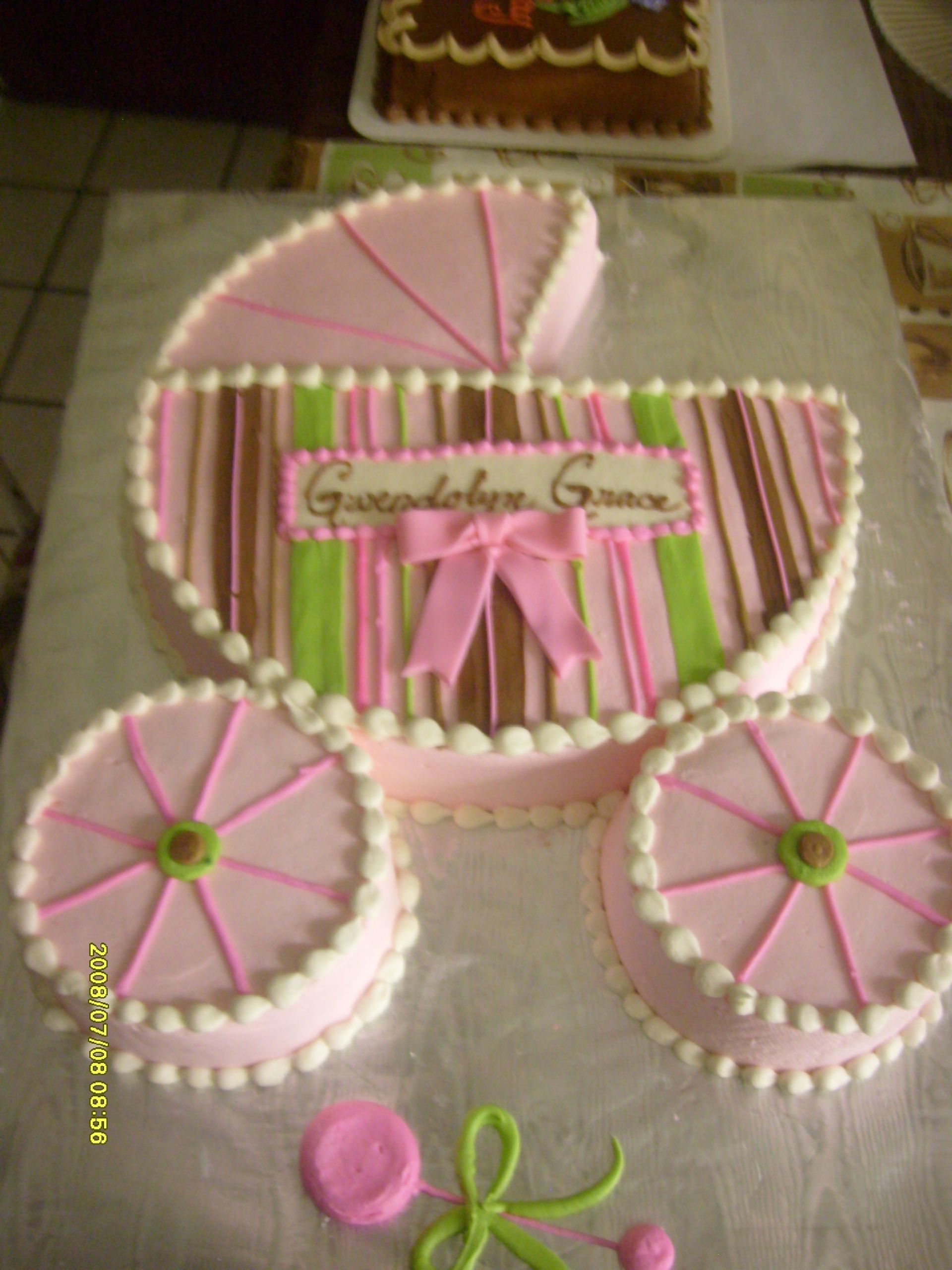 Pink baby carriage cake with white ruffles and ribbon bow on a table