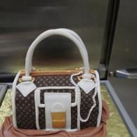 Brown and white designer handbag with a white handle and gold clasp on a display surface