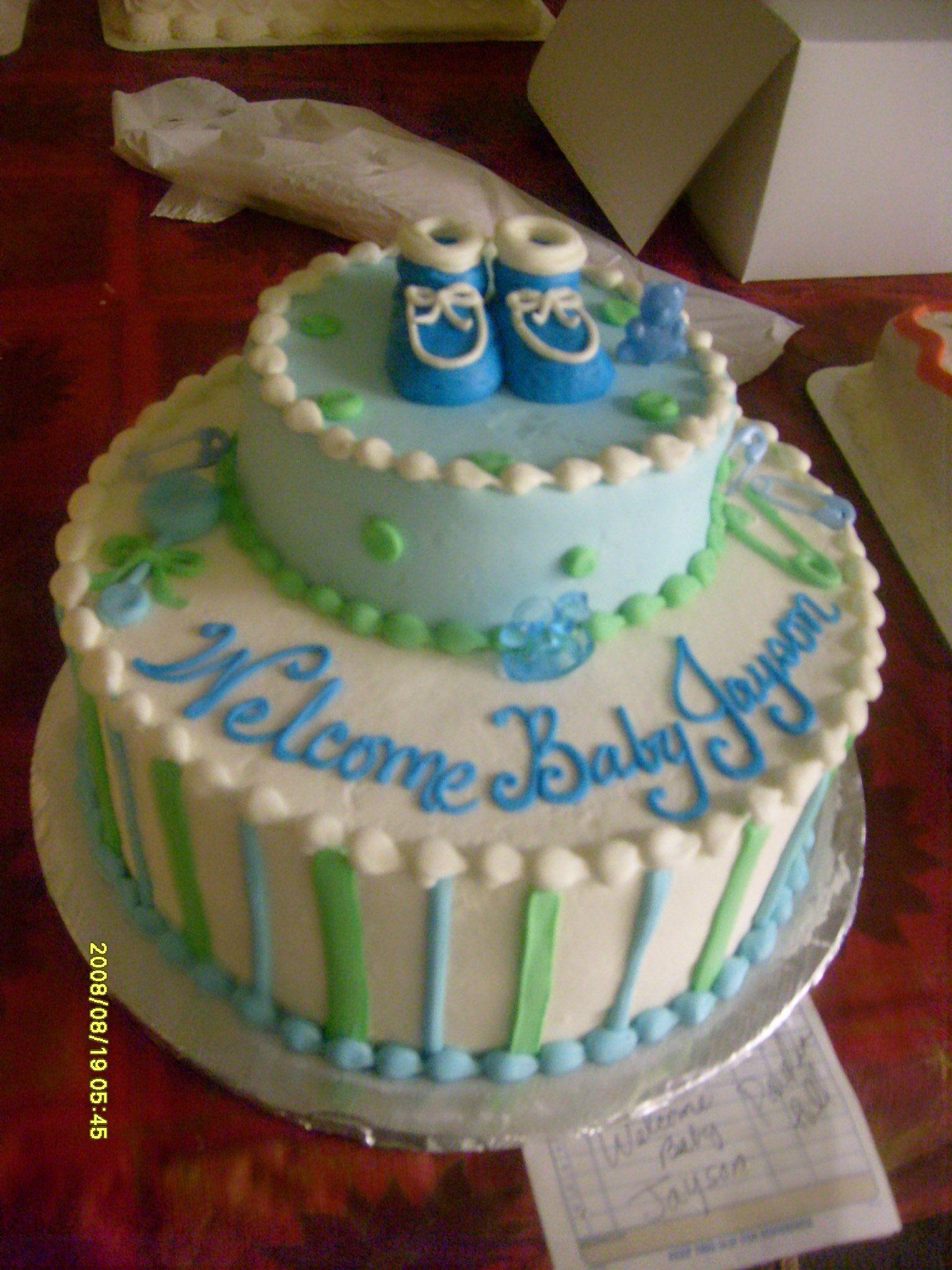Blue and white baby shower cake with “Welcome Baby Boy” icing and two baby bottle decorations