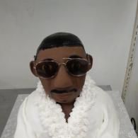 Small figure wearing round sunglasses and a fluffy white robe against a plain gray background