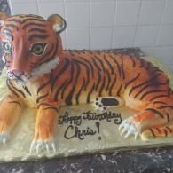 Tiger-shaped cake with orange-and-black stripes and Bengali writing on a plate