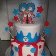 Two-tiered red, white, and blue birthday cake with star toppers and Dr. Seuss characters on top