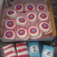 Box of decorated cupcakes with red, white, and blue icing, plus wrapped treats labeled 1 and 2.