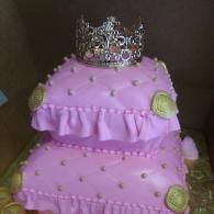 Pink two-tier cake with ruffled icing and a silver tiara topper