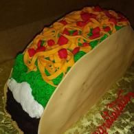 Taco-shaped cake with colorful icing toppings and green frosting on a table