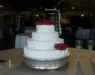 White tiered cake with red flowers on a silver stand at a reception table