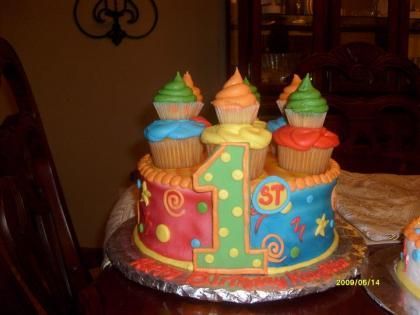 Colorful first-birthday cake with a large number 1 and icing cupcakes on top on a table