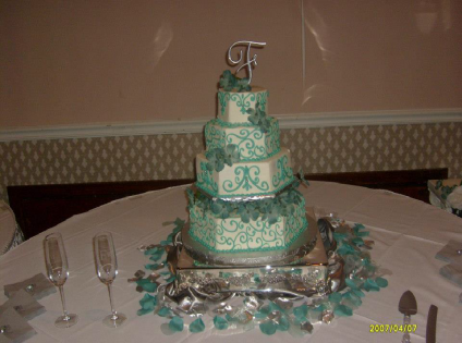 Tiered white-and-teal wedding cake on a decorated table with champagne flutes and silver accents