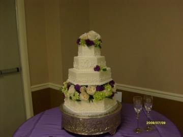 White tiered wedding cake with purple and white flowers on a table in a banquet room