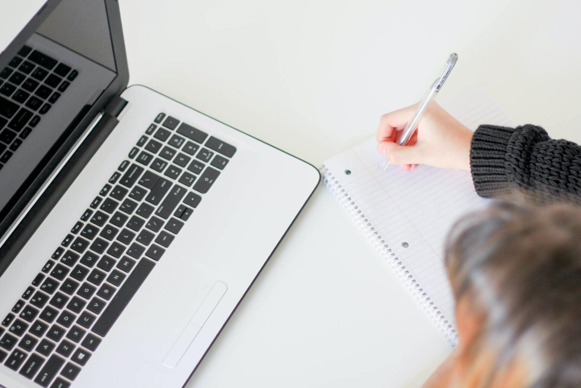 A person takes notes while looking at a laptop.