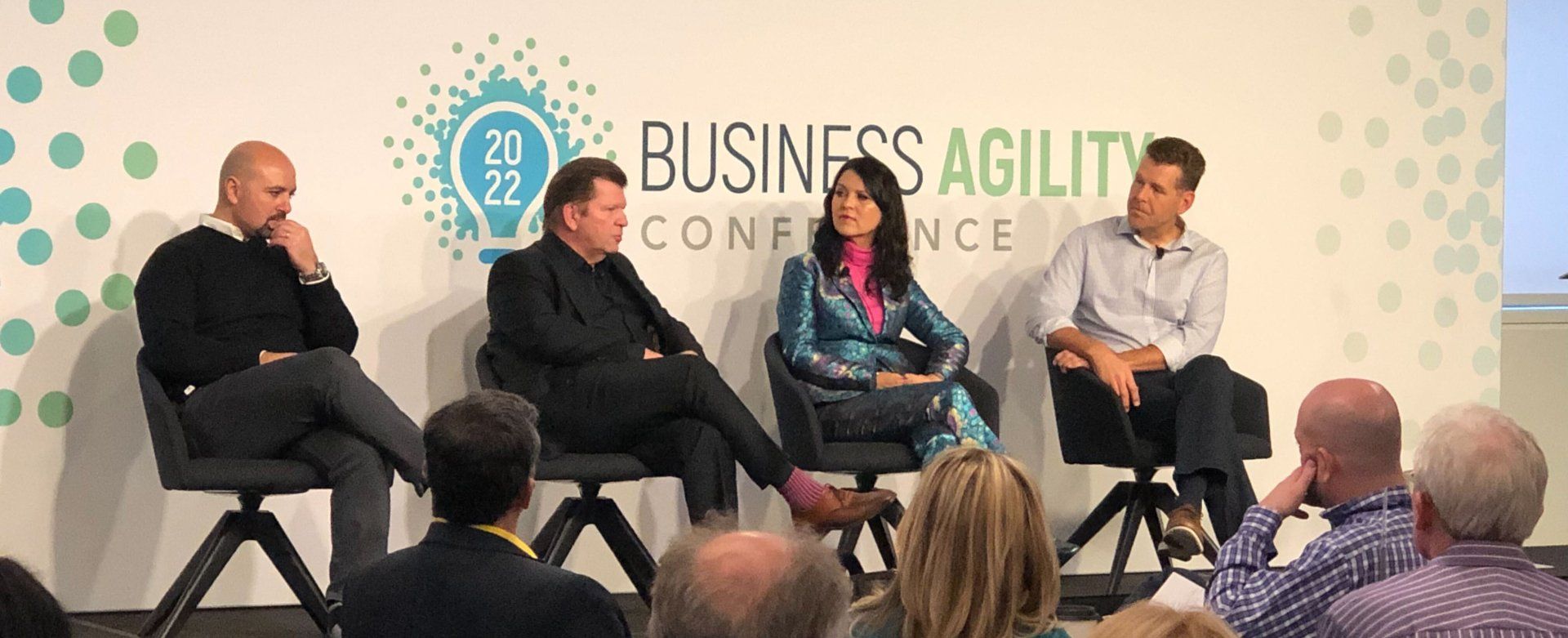 Three men and a woman sit on stage at the business agility conference