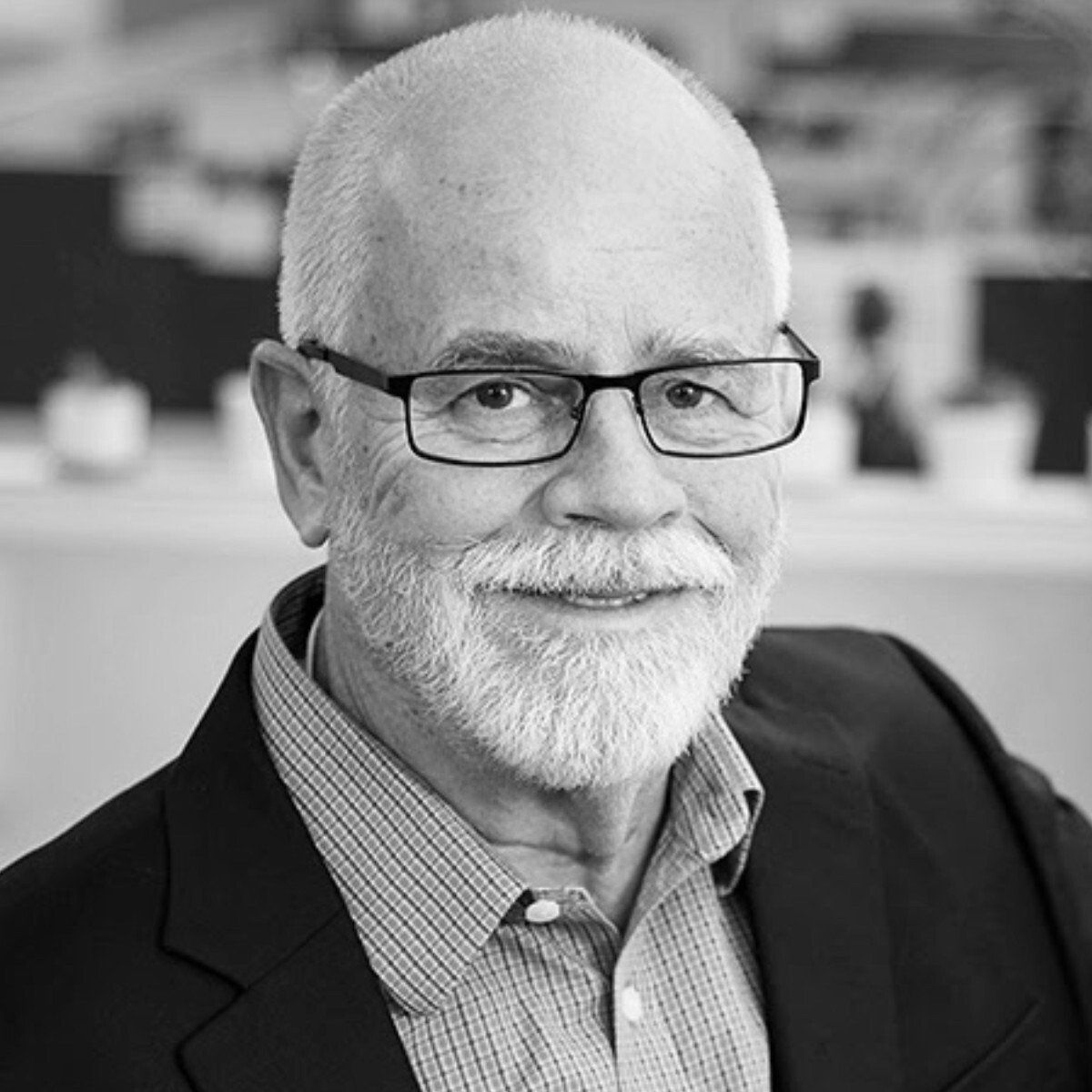 A man with a beard and glasses is wearing a suit and smiling in a black and white photo.