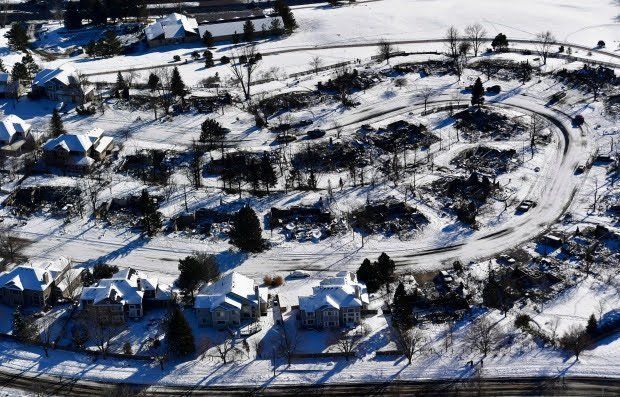 An aerial view of a neighborhood, mostly burned by fire. The ground is covered in snow