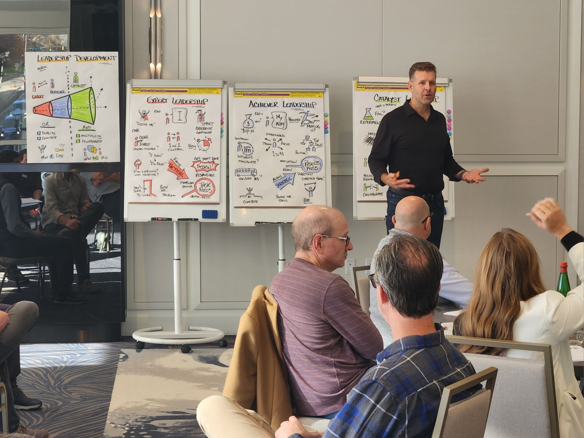 Man giving presentation at workshop with diagrams on whiteboards. Audience seated, attentive.