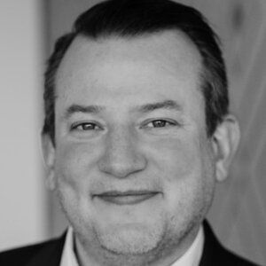 A man with a beard is smiling in a black and white photo.