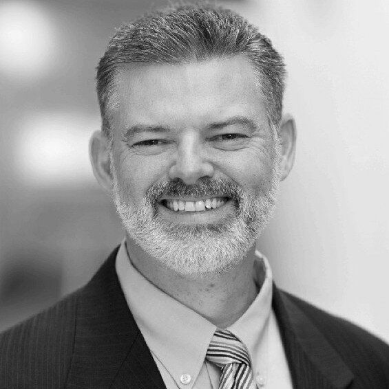 A man with a beard wearing a suit and tie is smiling in a black and white photo.