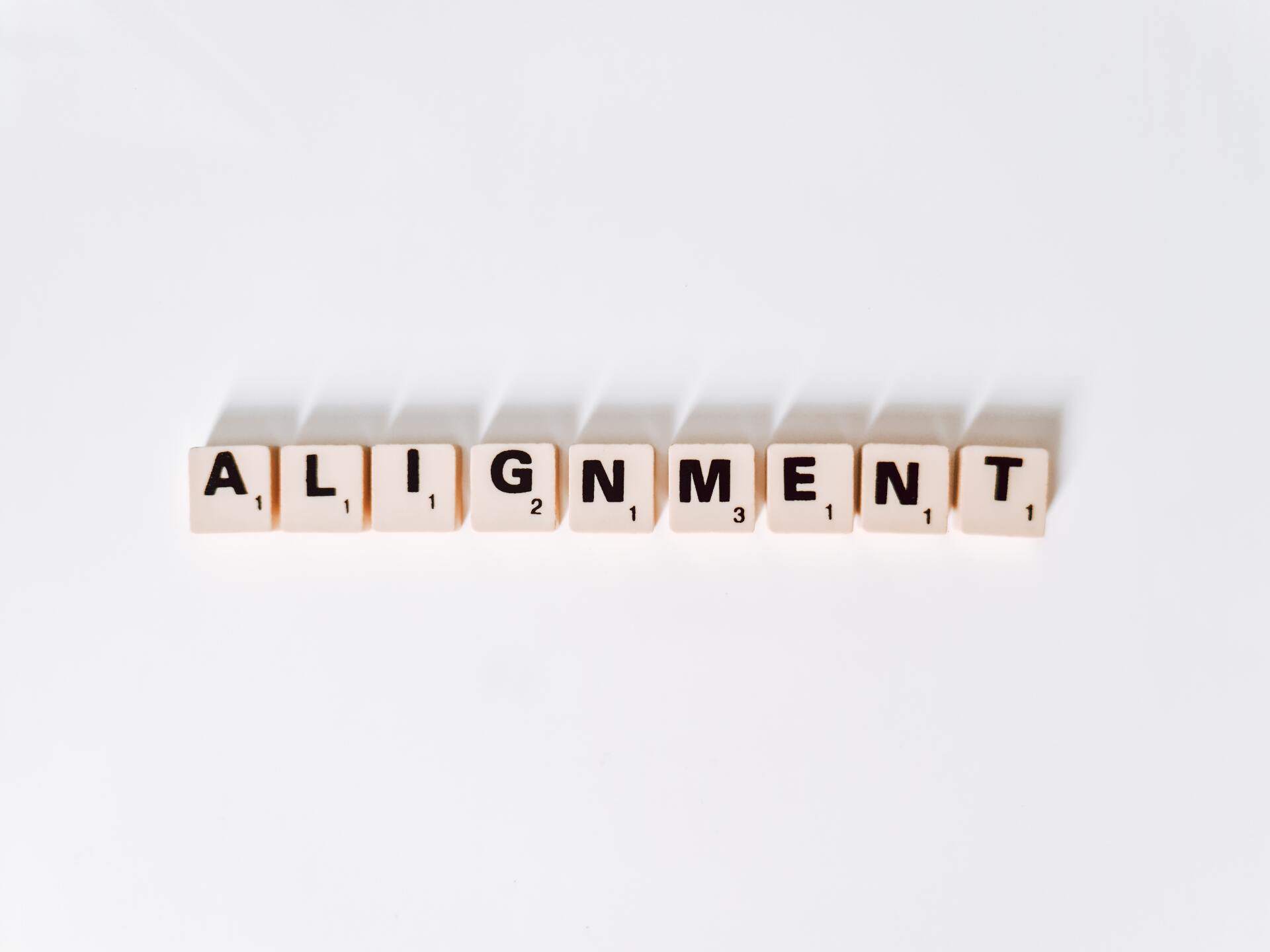 Wood tiles that spell out the word, Alignment, on a white surface