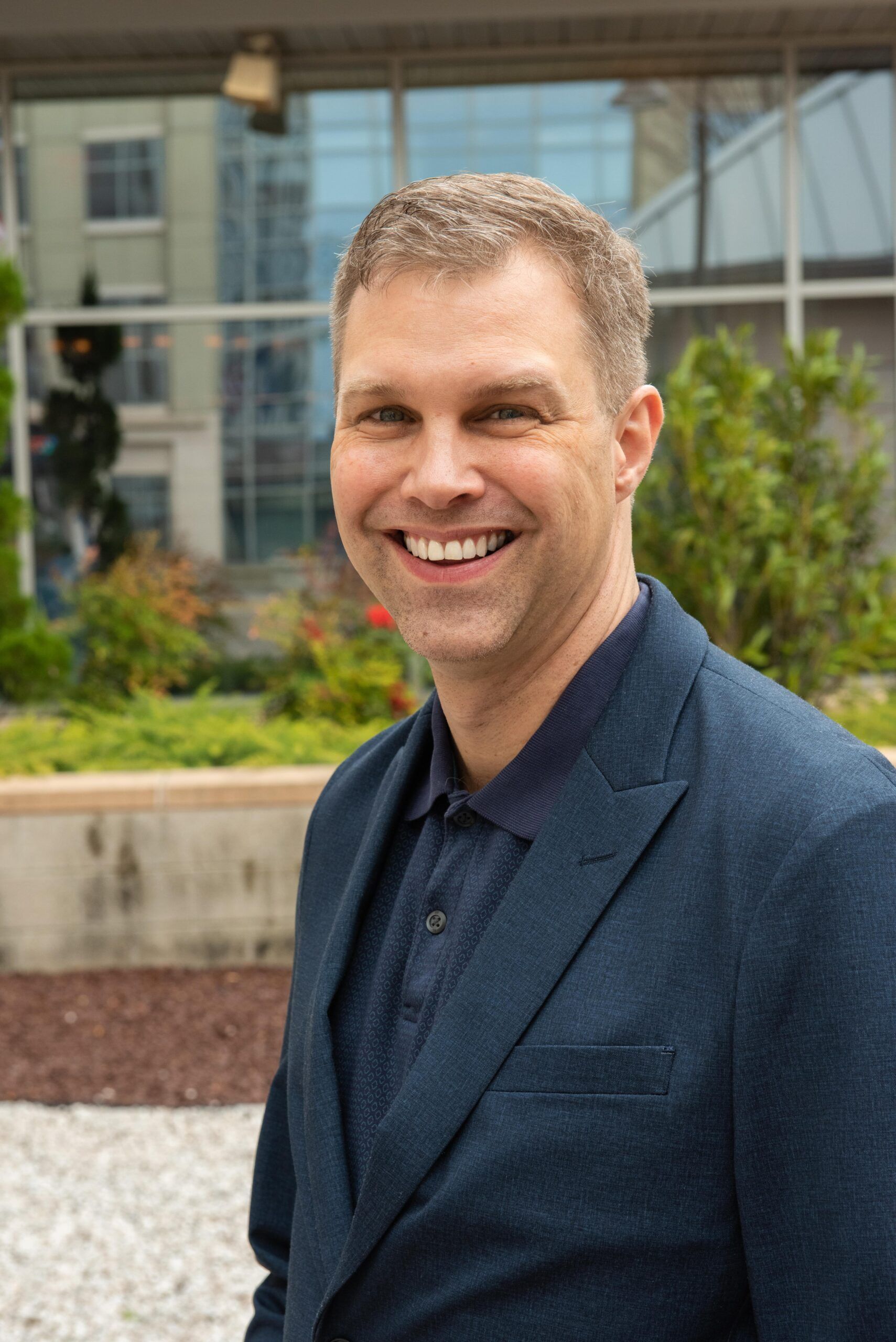 A man in a suit is smiling for the camera while standing in front of a building.