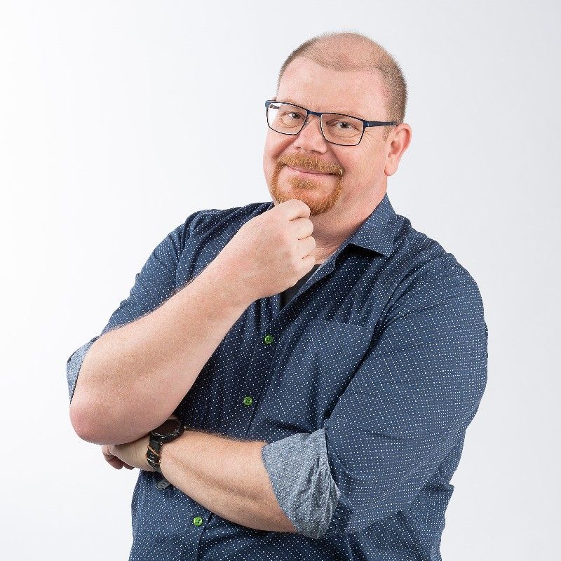 A man wearing glasses and a blue shirt is standing with his arms crossed.