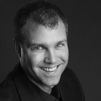 A man in a suit and tie is smiling in a black and white photo.