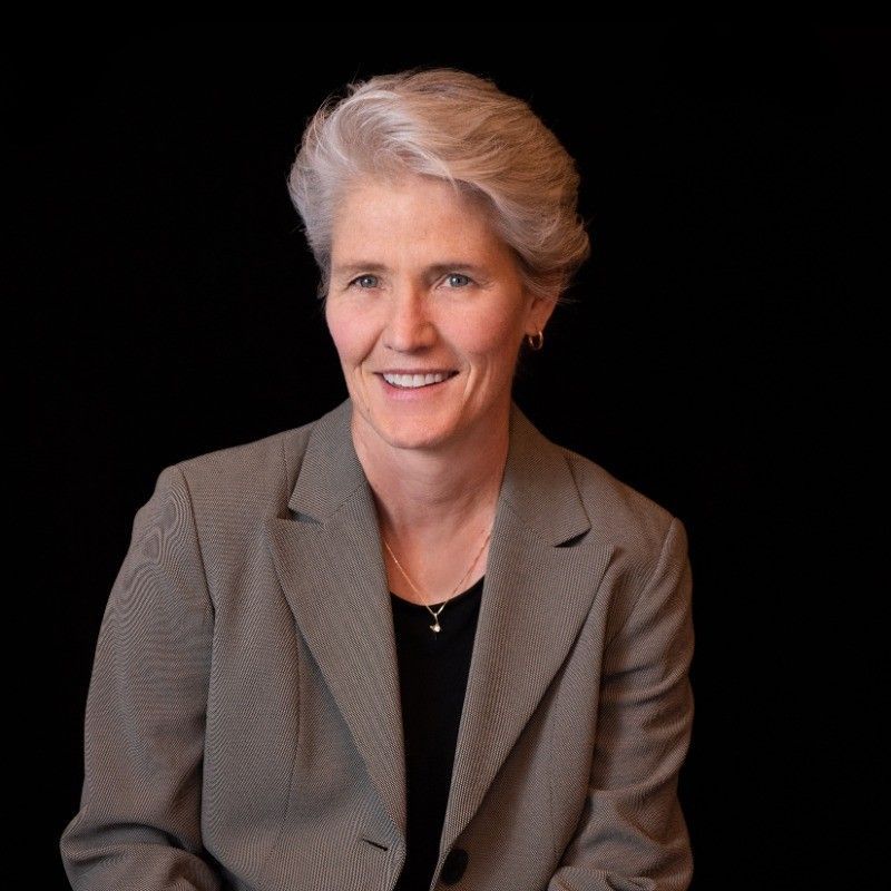 A woman wearing a grey jacket and black shirt smiles for the camera