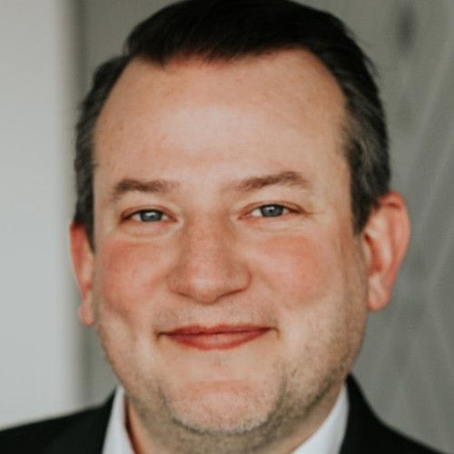 A man in a suit and white shirt is smiling for the camera.