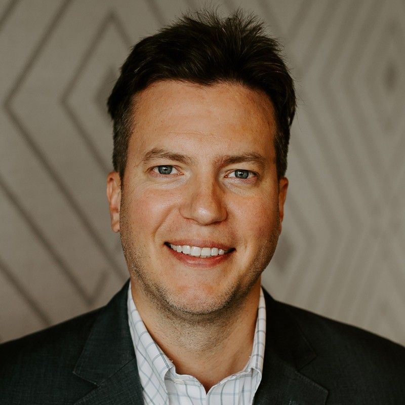 A man in a suit and plaid shirt is smiling for the camera.