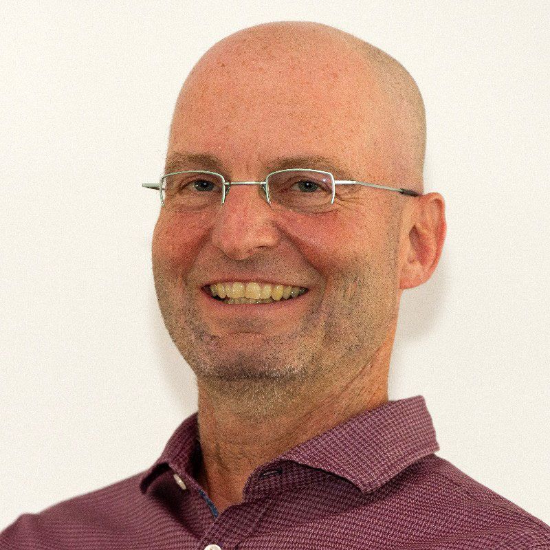 A bald man wearing glasses and a purple shirt is smiling.
