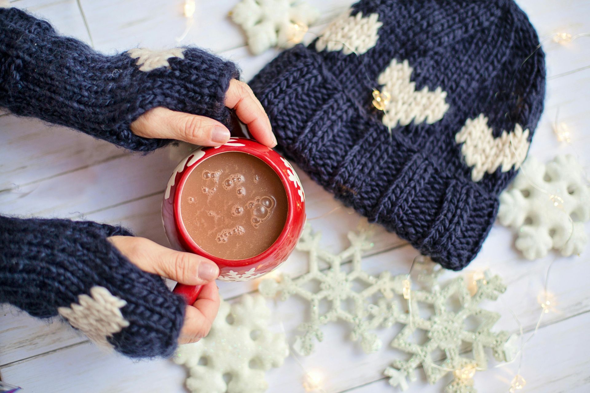 A person is holding a cup of hot chocolate next to a hat and snowflakes.