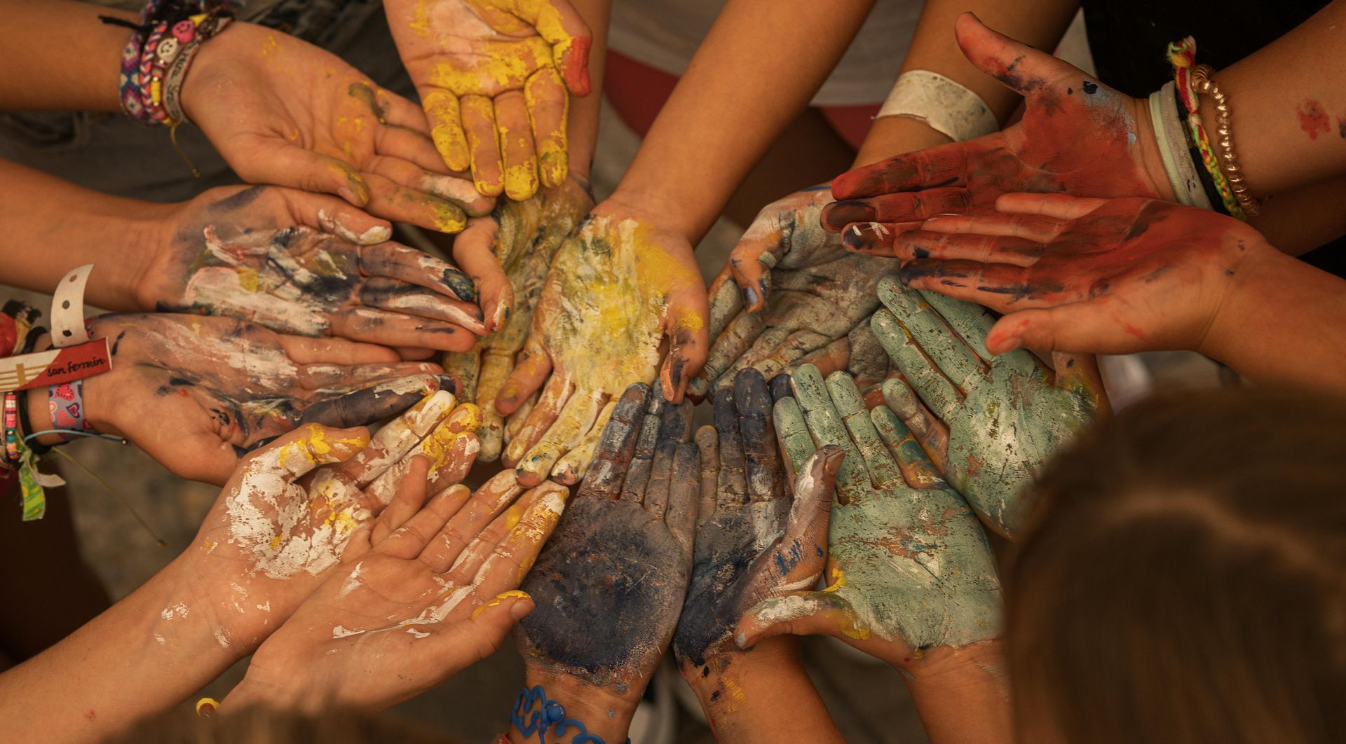 many hands in a circle with paint on them depicting the feeling of leading through the messy middle