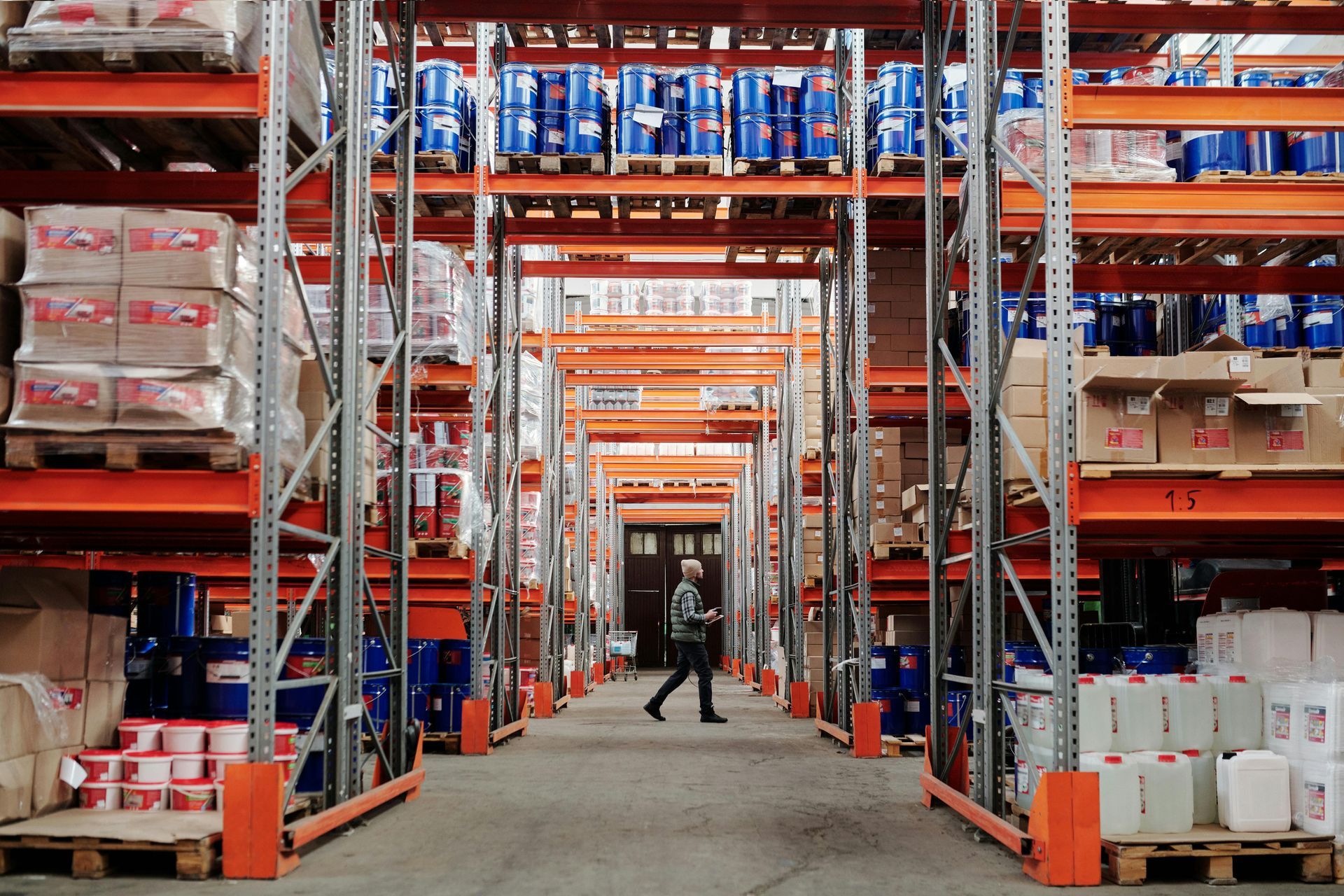 A man is walking through a large warehouse filled with lots of shelves.